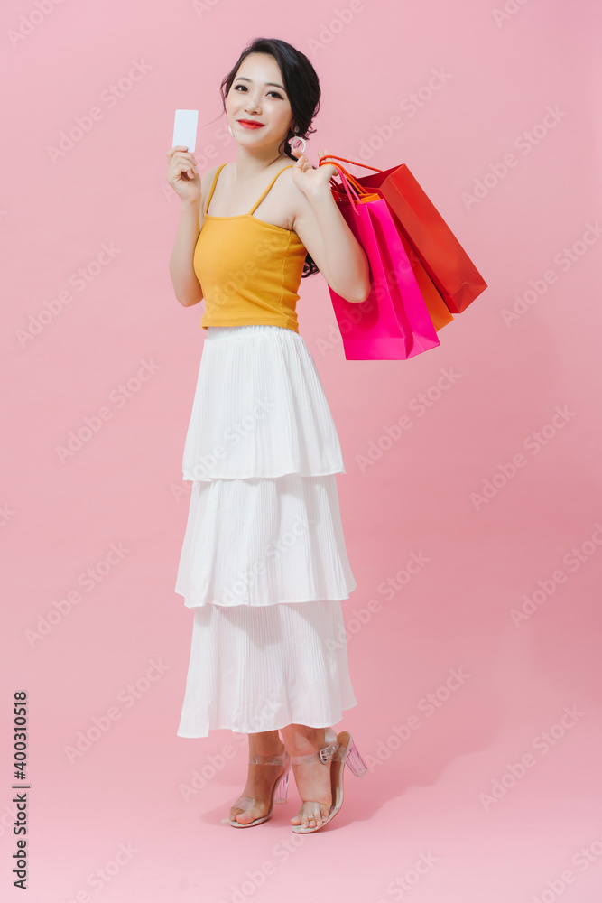 Happy Shopaholic. Portrait Of Joyful Asian Girl With Colorful Shopping Bags And Credit Card Isolated Over pink Background