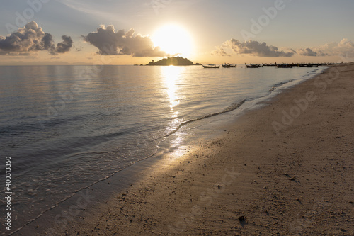 Selective focus of a peaceful beach during sun rise with golden light and blue sky. Fishing boat background