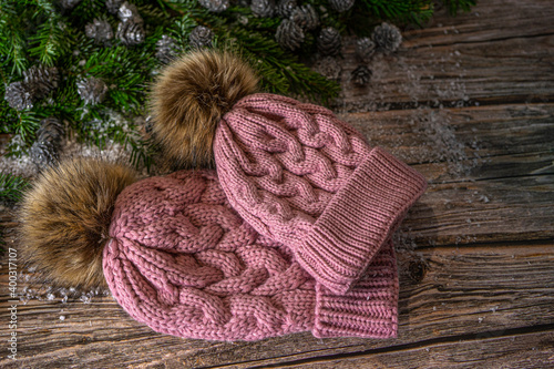 Warm knitted pink hats with pompom for mother and daughter. Christmas decoration on wooden background.