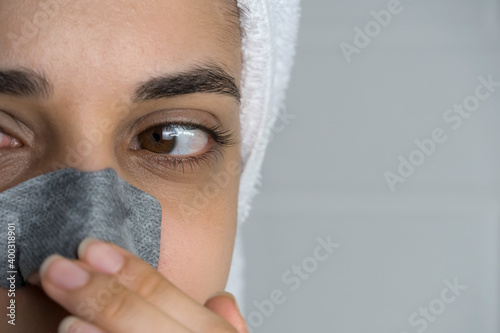 A woman sticks a cleansing strip on her nose. Black dots on the nose. Girl without makeup in the bathroom. Skin care  problem skin  cleansing. Natural beauty  naturalness. Blackheads and comedones.