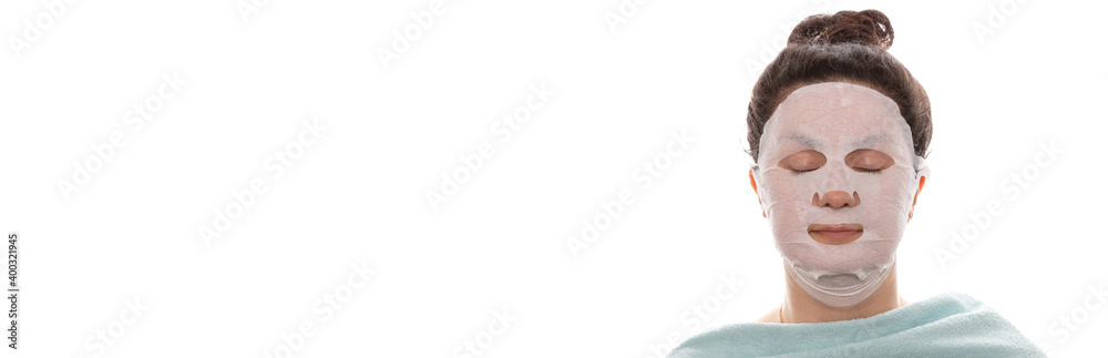 Face care and beauty treatments. Woman with a moisturizing mask on her face isolated on white background. Eyes closed, shoulders covered with towel. Health care, spa concept. Banner size. Copy space