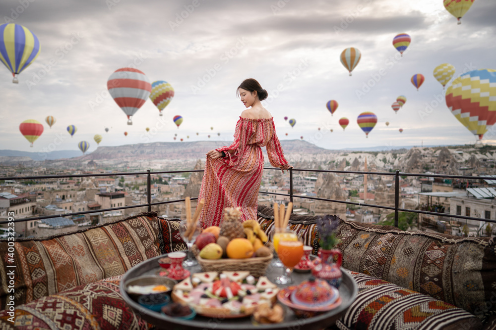 Happy women on rooftop of cave house enjoying of Goreme city panorama, Cappadocia Turkey. 3D balloons in the sky. - obrazy, fototapety, plakaty 