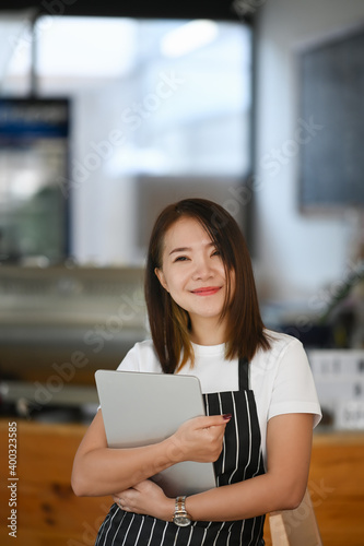 Portrait of cheerful young female entrepreneur smiling and standing welcomingly at her modern cafe.