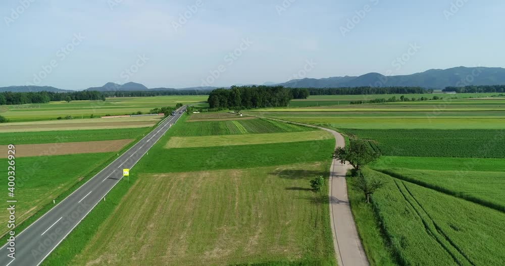 Drone aerial view of green farming grassland fields. Countryside road between agriculture fields. Local paved path for walking and cycling. Forward dolly moving Drone aerial view of green farming grassland fields. Countryside road between agriculture fields. Local paved path for walking and cycling. Forward dolly moving