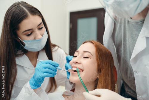 Gloved technicians examine a smiling client's teeth using a dental mirror