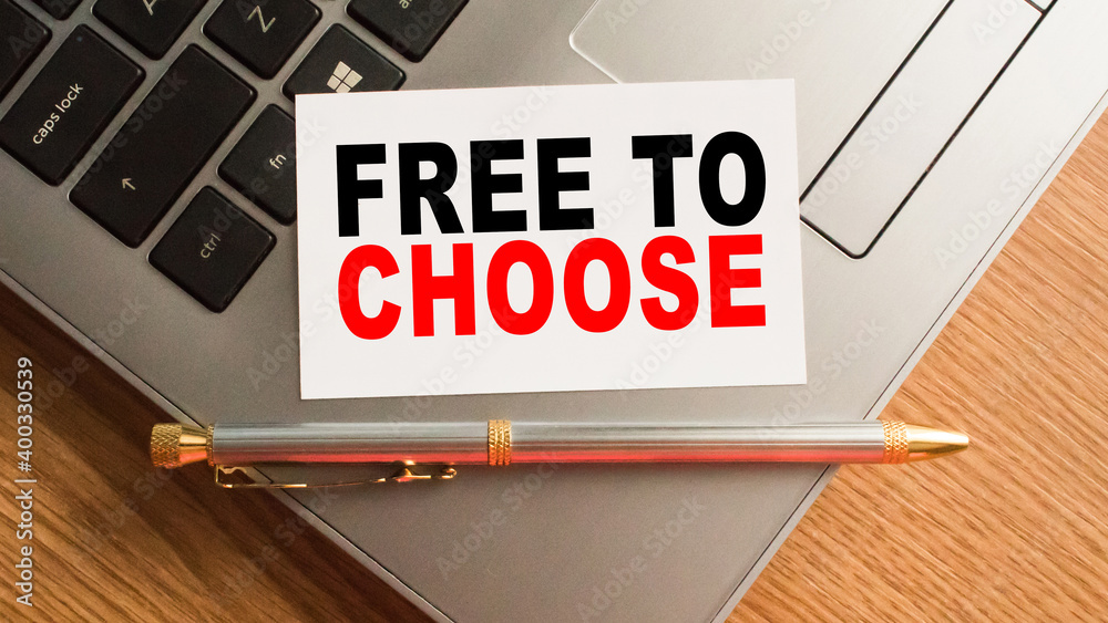 Notepad with the text FREE TO CHOOSE is on the laptop keyboard. Minimal work space. Business concept.