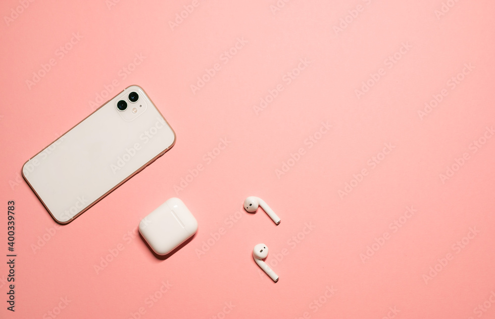 Simple flat lay photo on a pastel pink background with a white smartphone and wireless earphones with a charging case. Simple flat lay photo on a pastel pink background with a white smartphone and wireless earphones with a charging case.