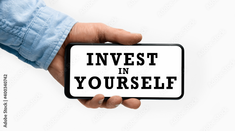 Closeup of a male hand holding Smartphone with text INVEST IN YOURSELF on display Closeup of a male hand holding Smartphone with text INVEST IN YOURSELF on display