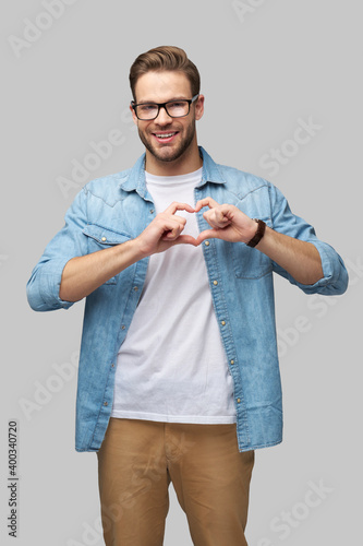 Portrait of handsome young caucasian man making heart sign by hands over grey background