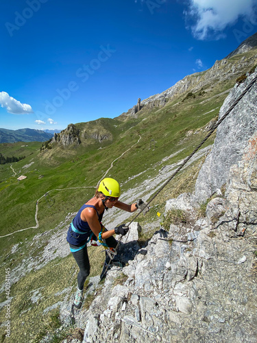 Pretty female climber on a steep Via Ferrata in the Swiss Alps - fearlessly climbing higher on this extreme alpine trail photo