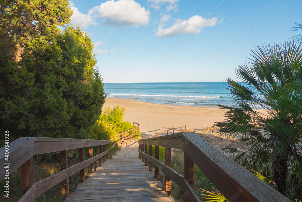 Wooden boardwalk overlooking the sea. Beautiful promenade leading the playa Romana on a sunny summer day. Alcossebre, Valencian Community, Castellon province, Spain.