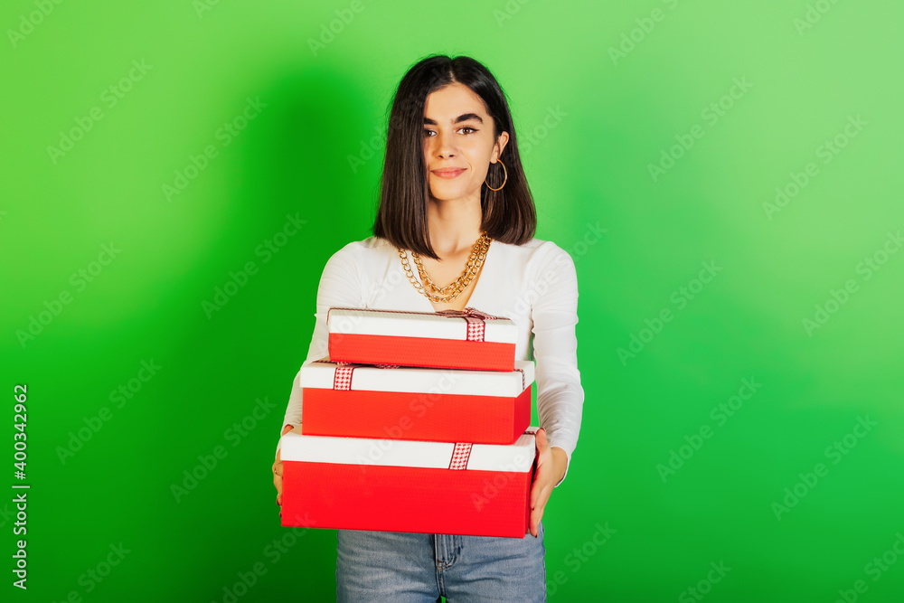 Smiling young girl holding pile of gifts and looking at camera while standing on green background. Holiday, Birthday, Christmas, Valentine's Day or Women's Day. Smiling young girl holding pile of gifts and looking at camera while standing on green background. Holiday, Birthday, Christmas, Valentine's Day or Women's Day.