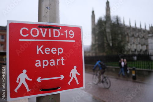 Red sign saying Keep Apart, refering to mandatory social distancing in the united kingdom beacuse of the coronavirus outbreak. Out of focus church in the background, symbol of Cambridge city