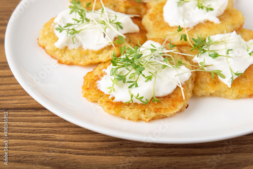 Potato pancakes with sour cream and watercress microgreens on wooden textured table