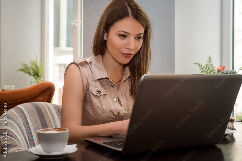 Young beautiful smiling brunette woman works on laptop in cafe