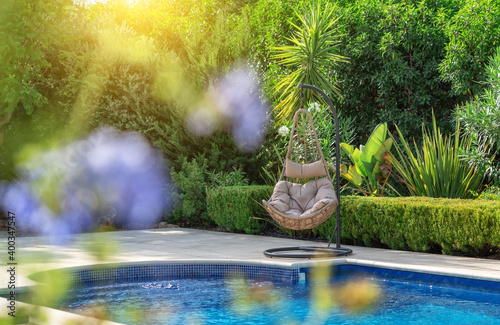Luxurious pool in the garden of a private villa, hanging chair with pillows for leisure tourists, in summer. Portugal, Algarve.