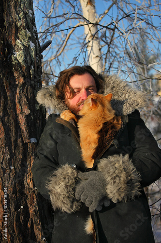 a bearded man with a red cat on the background of a winter forest