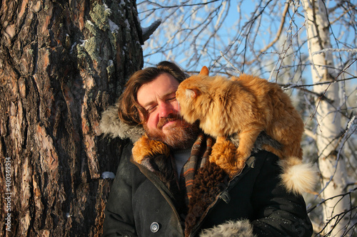 a bearded man with a red cat on the background of a winter forest