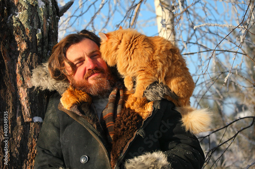 a bearded man with a red cat on the background of a winter forest