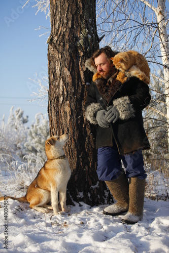 a bearded man with a red cat on the background of a winter forest