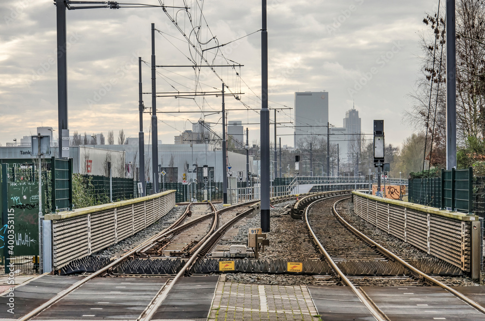 Rotterdam, The Netherlands, December 13, 2020: level crossing of a suburban street and a metroline with the downtown highrise in the background