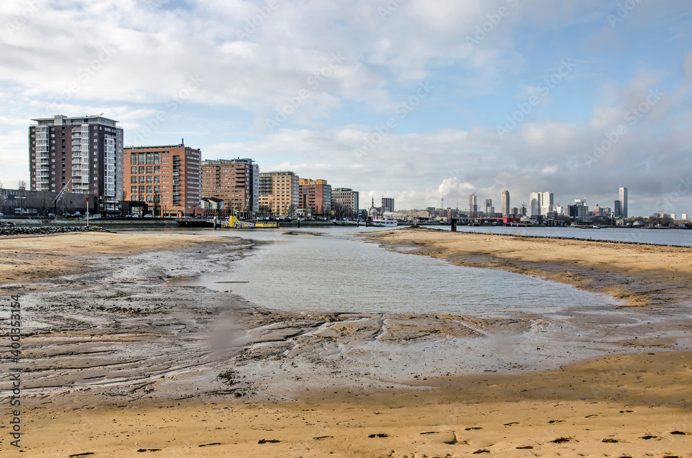 Rotterdam, The Netherlands, December 17, 2020: newly created sandy and muddy beach on Brienenoord island, with a row of apartment buildings and the city's skyline in the background Rotterdam, The Netherlands, December 17, 2020: newly created sandy and muddy beach on Brienenoord island, with a row of apartment buildings and the city's skyline in the background