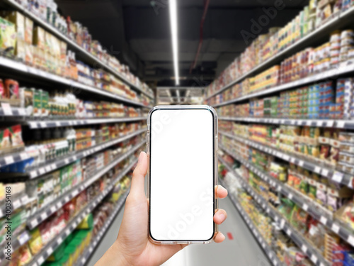 Woman holding blank white screen smartphone at supermarket with blur background, shopping concept, technology concept.