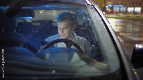 Portrait of man in electric car typing on smartphone happy and smiling. Handsome male sitting in vehicle in good mood and texting on mobile phone. Transport , taxi driver, night