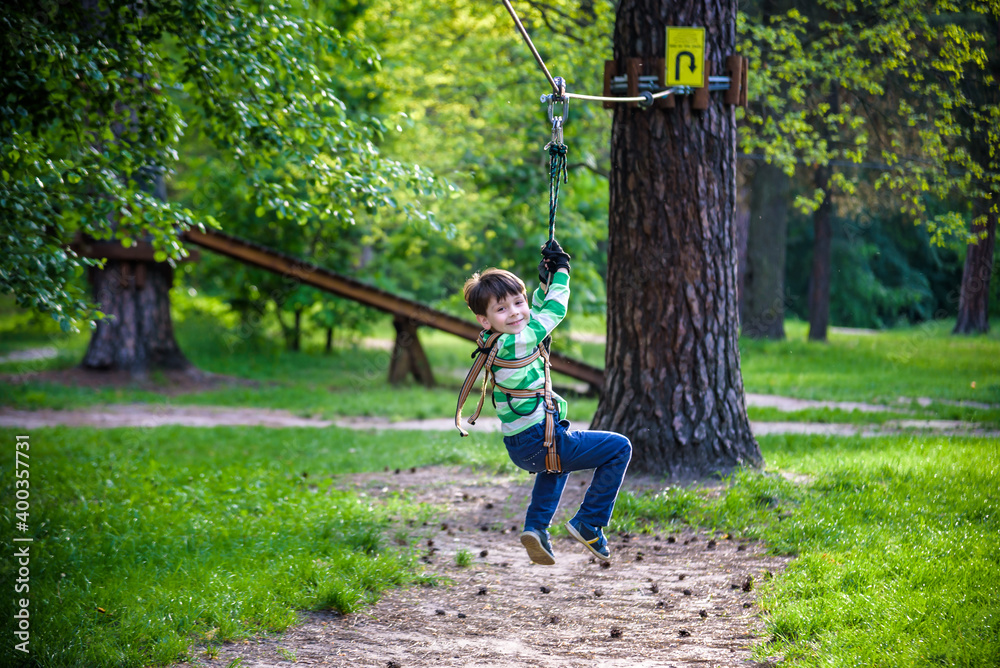 Fototapeta premium smiling boy rides a zip line. happy child on the zip line. The kid passes the rope obstacle course