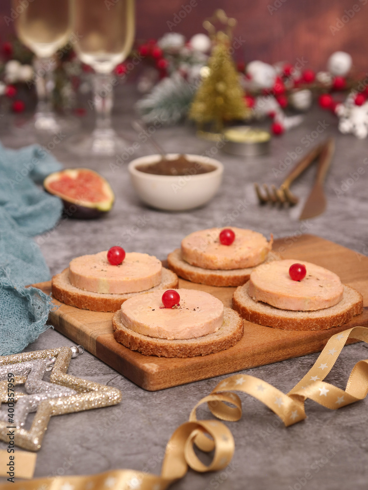 A French traditional foie gras topped on toaster bread on a wooden plate aside with onion marmalade and a piece of fig fruit,  glasses of Champagne in background, with Christmas atmosphere decoration.