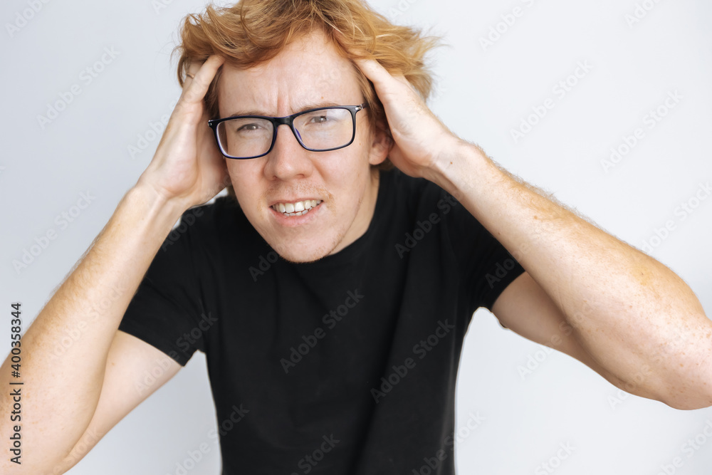 Red-haired man with glasses holding his head on a white background in a black T-shirt Red-haired man with glasses holding his head on a white background in a black T-shirt