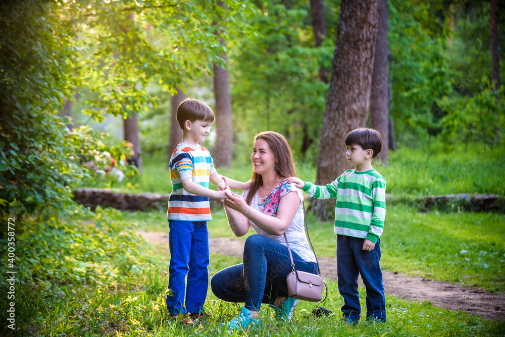 Fototapeta premium Young woman mother applying insect repellent to her two son before forest hike beautiful summer day or evening. Protecting children from biting insects at summer. Active leisure with kids