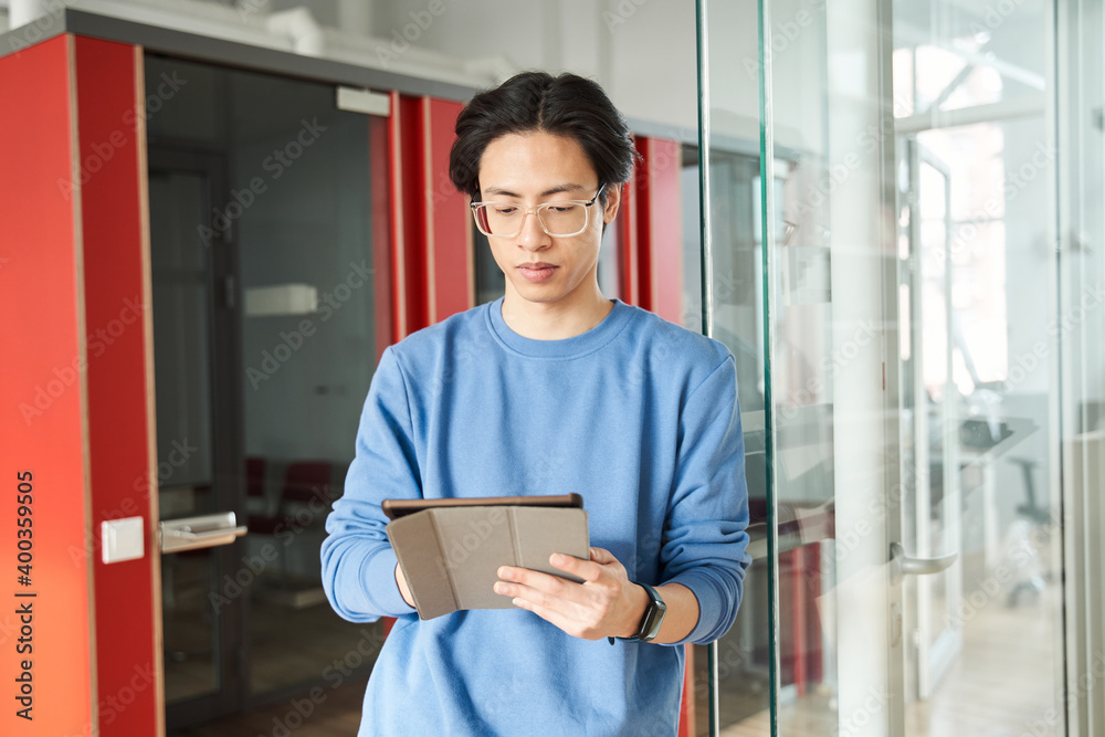 Photo of thinking multiracial man wearing eyeglasses typing on his tablet computer Photo of thinking multiracial man wearing eyeglasses typing on his tablet computer