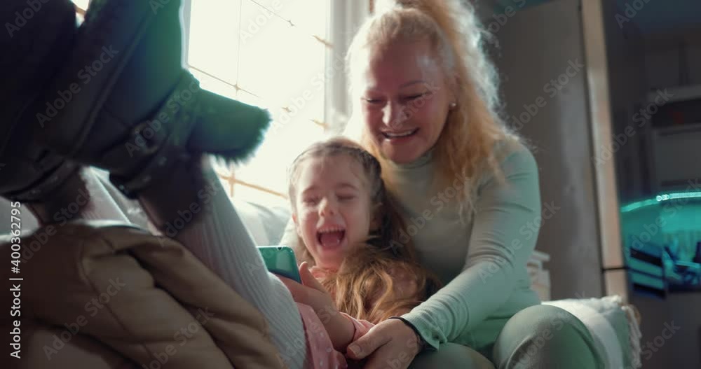 Happy grandmother and her cheerful little granddaughter are enjoying a family video call. Happy family in quarantine. The young grandmother uses smartphones. Stay at home. Happy grandmother and her cheerful little granddaughter are enjoying a family video call. Happy family in quarantine. The young grandmother uses smartphones. Stay at home.