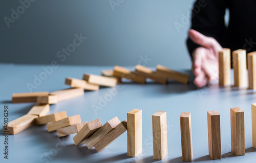 Close up of businessman hand Stopping Falling wooden Dominoes effect from continuous toppled or risk, strategy and successful intervention concept for business.