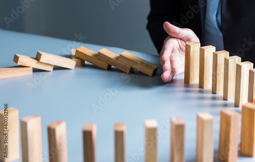 Businessman hand stop dominoes continuous toppled or risk with copyspace. Business risk, strategy and planing concept idea.