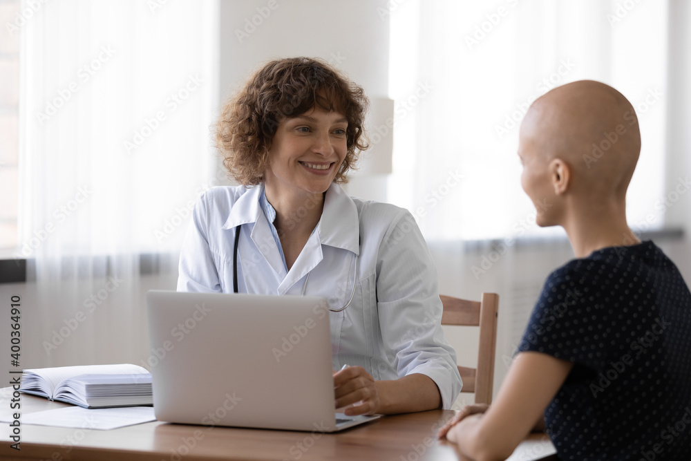 Obraz premium Young ill woman having cancer diagnosis visit attending physician at clinic. Happy friendly female doctor oncologist consult patient glad to mention good therapy result inform about reaching remission