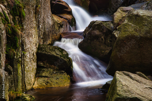 Autumn long exposure of creek Black  Big  Stolpich waterfalls in Jizera Mountain. Water falls into a deep forest canyon full of granite stones and rocks covered with green moss. Czech Republic