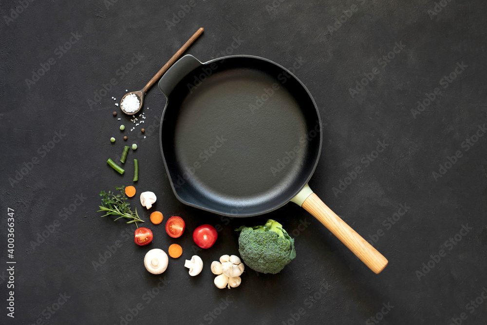 Cast iron frying pan with vegetables, spices and herbs on a black background. Cast iron frying pan with vegetables, spices and herbs on a black background.