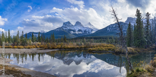 Tableau sur toile Snow capped The Three Sisters trio peaks mountain with blue sky and white clouds reflect on water surface in autumn
