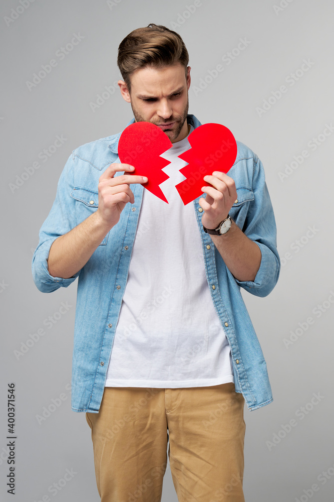 Fototapeta premium handsome young man holding broken paper red valentine heart standing over grey background