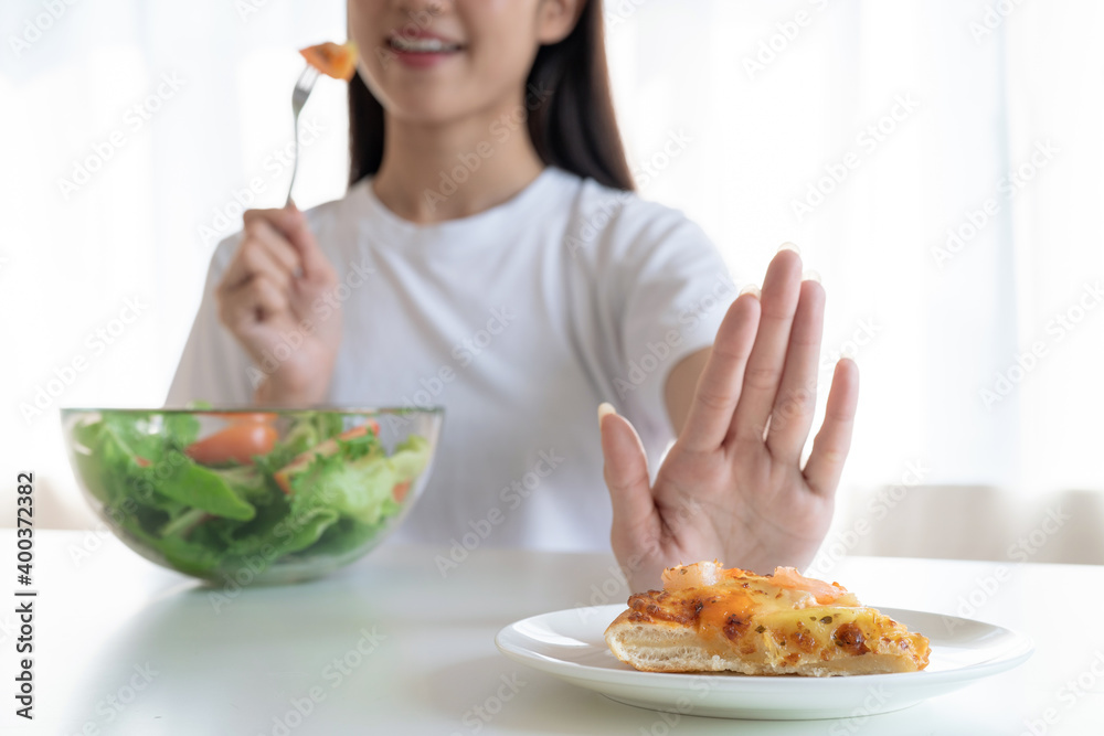 Young Asian woman pushes her favorite pizza with her hand and choose to eat a healthy vegetable salad. Young Asian woman pushes her favorite pizza with her hand and choose to eat a healthy vegetable salad.