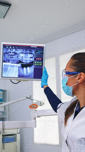 Dentist doctor and patient looking at digital teeh x-ray in dental office  person pov. Stomatology wearing protective face mask and gloves pointing at teeth radiography in stomatological clinic