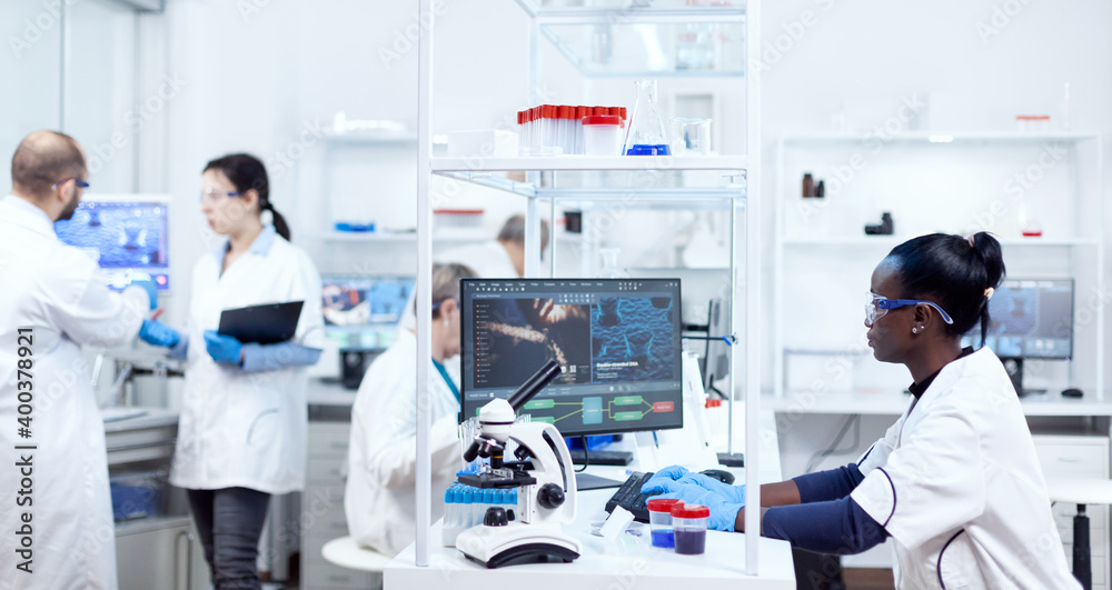 African scientist sitting at her workplace in modern facility for medicine industry. Black healthcare researcher in biochemistry laboratory wearing sterile equipment.