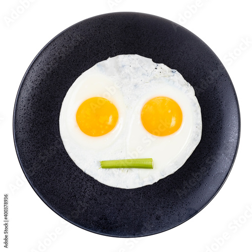 top view of fried eggs and piece of celery on black plate isolated on white background. Fried eggs like face with straigh closed mouth