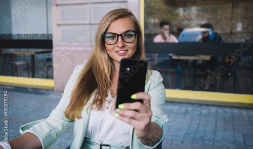 Elegant woman with phone taking selfie in outdoor cafe