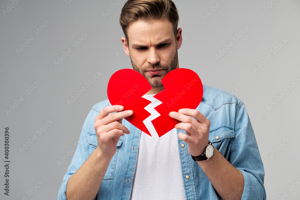 handsome young man holding broken paper red valentine heart standing over grey background handsome young man holding broken paper red valentine heart standing over grey background