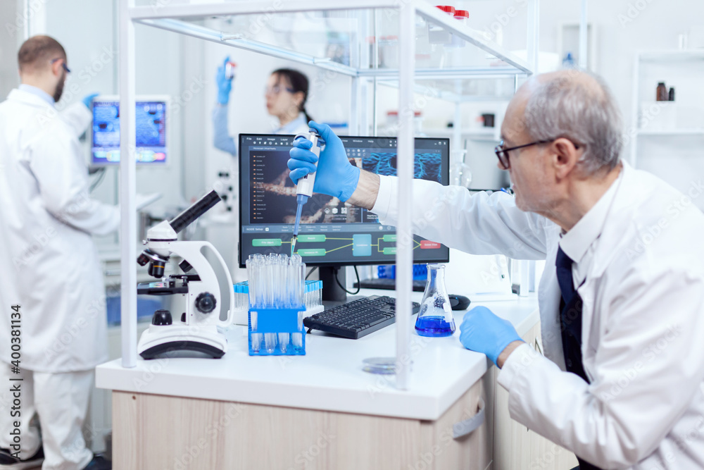 Healthcare specialist in chemistry laboratory doing scientific research with dropper dispenser. Senior professional chemist using pippete with blue solution for microbiology tests. Healthcare specialist in chemistry laboratory doing scientific research with dropper dispenser. Senior professional chemist using pippete with blue solution for microbiology tests.