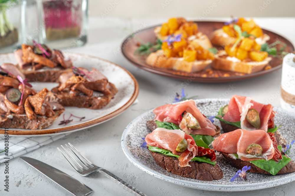 Bruschetta with prosciutto and various ingredients on plates served on the table, close up