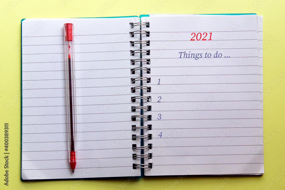 2021 and the phrase things to do written on a notebook, with a red pen on, on yellow background . selective focus 2021 and the phrase things to do written on a notebook, with a red pen on, on yellow background . selective focus